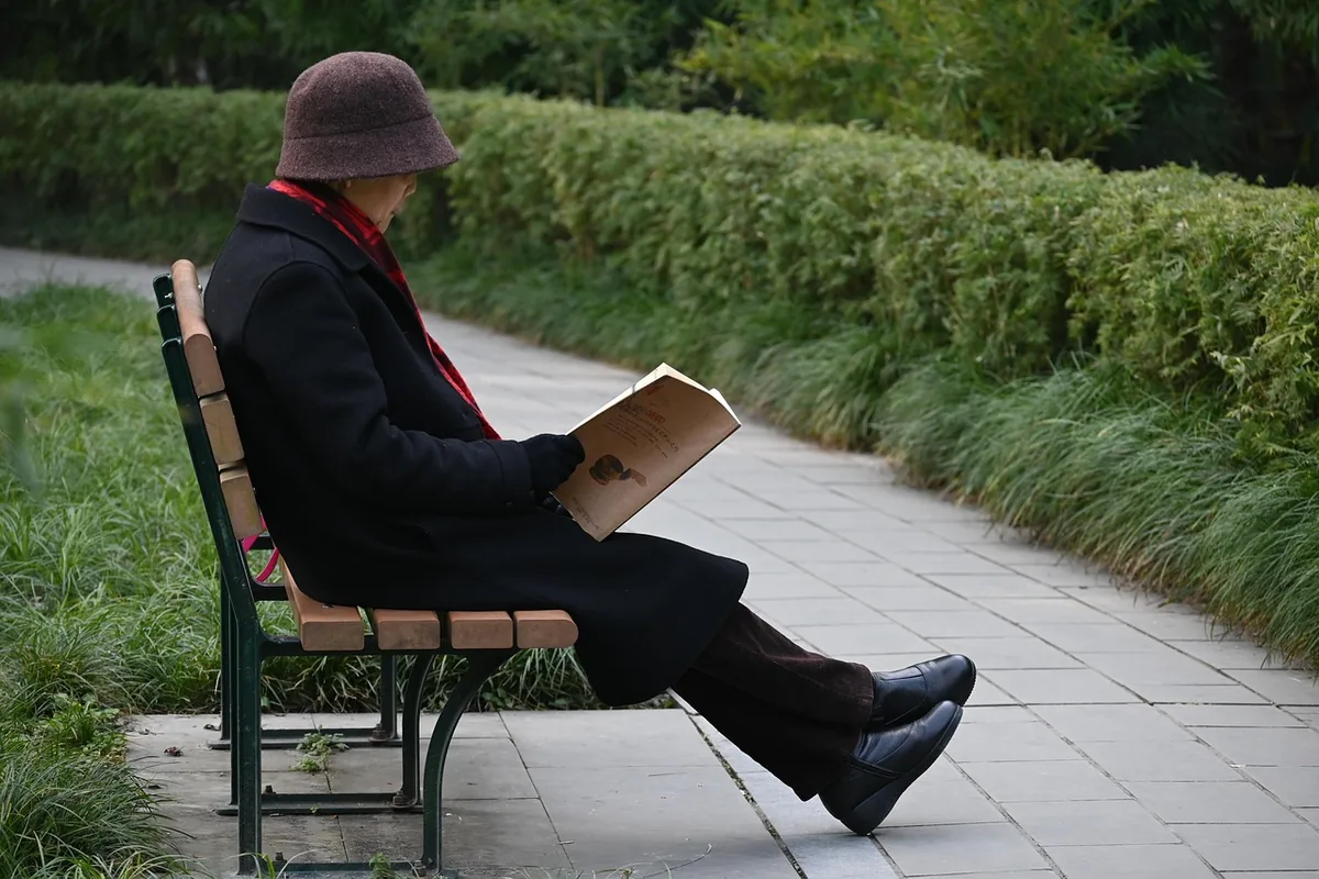 An older adult reading a book alone on a park bench